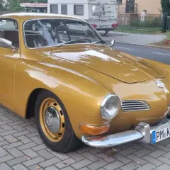 Złoty Karmann Ghia, klasyk z lat 60., lśni na tle ulicy.