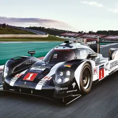 Porsche 919 Hybrid pędzi po torze wyścigowym, oznaczony numerem 1, w barwach czarno-białych z flagą Niemiec.