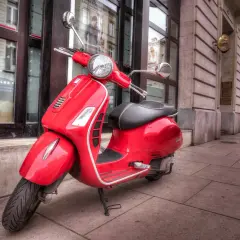 Czerwony skuter Vespa na chodniku. Zastanawiasz się, ile kosztuje prawo jazdy AM?