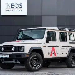 Beżowy INEOS Grenadier z czerwonym logo "A" na drzwiach. Sprawdź INEOS Grenadier cena i możliwości tego terenowego SUV-a.
