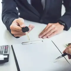 Przekazanie kluczyków do samochodu po podpisaniu umowy leasingu finansowego. Obok kalkulator i pieniądze.