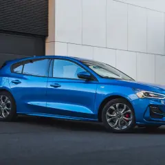 Błękitny hatchback Ford Focus stoi przed nowoczesnym budynkiem.