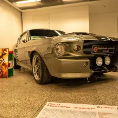 Szary Ford Mustang „Eleanor” z filmu „60 sekund” obok plakatu z Nicolasem Cage'em.