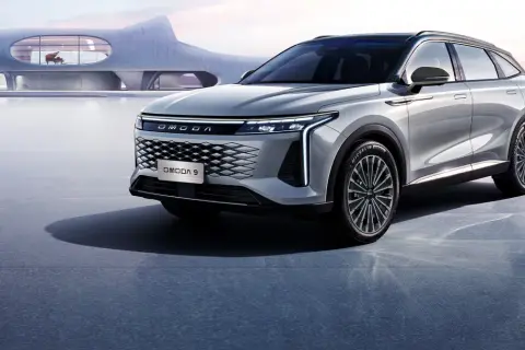 Elegancki, srebrny SUV OMODA 9 na tle futurystycznego budynku z fortepianem.