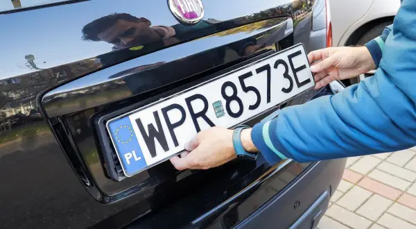 Ręce montują tablicę rejestracyjną WPR 8573E. To może być duplikat tablicy rejestracyjnej, gdy oryginał zaginął.