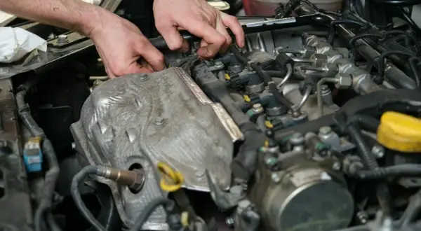 Mechanik wymienia czujnik położenia wałka rozrządu w silniku samochodowym.