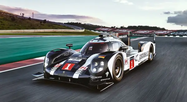 Porsche 919 Hybrid pędzi po torze wyścigowym, oznaczony numerem 1, w barwach czarno-białych z flagą Niemiec.