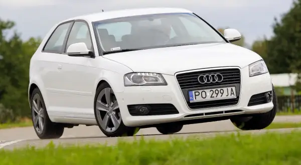 Białe Audi A3 8P 1.6 MPI na zakręcie. Kierowca w środku. Opinie o tym modelu są różne, ale wygląd zachwyca.