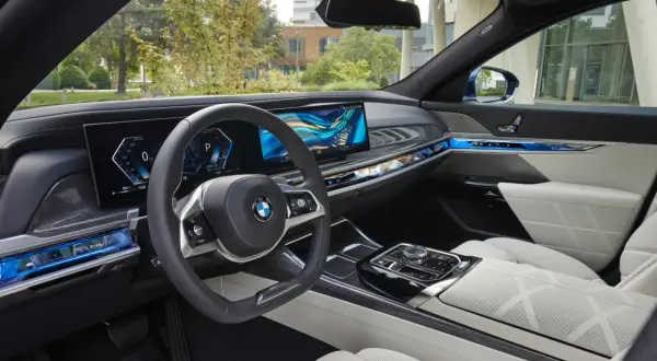 Wnętrze BMW 740d z nowoczesnym panelem cyfrowym, podświetlanymi detalami i komfortowymi, białymi fotelami.