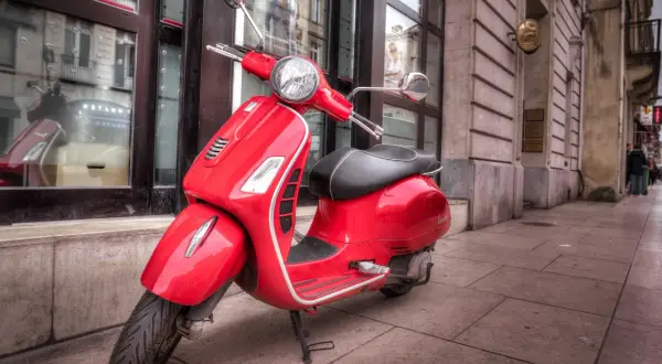 Czerwony skuter Vespa na chodniku. Zastanawiasz się, ile kosztuje prawo jazdy AM?