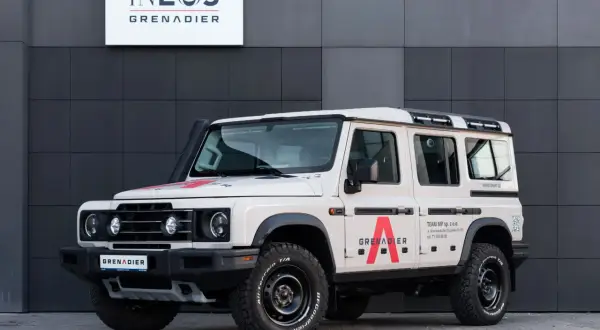 Beżowy INEOS Grenadier z czerwonym logo "A" na drzwiach. Sprawdź INEOS Grenadier cena i możliwości tego terenowego SUV-a.