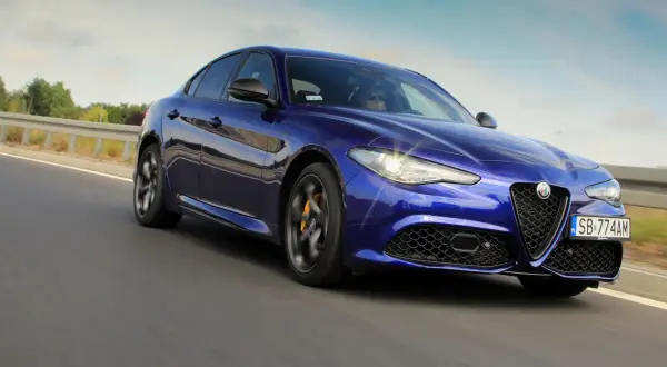 Błękitne Alfa Romeo Giulia Veloce pędzi po drodze, błyszcząc w słońcu.