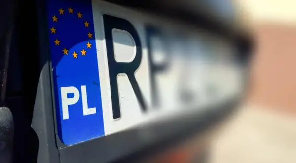 Zbliżenie na polską tablicę rejestracyjną z symbolem Unii Europejskiej. Litery "PL" i fragment numeru wskazują na cg rejestracja.