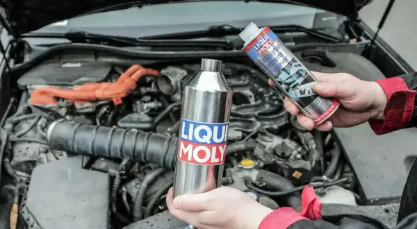 Dwie ręce trzymają produkty Liqui Moly do czyszczenia katalizatora. W tle widać silnik samochodu.