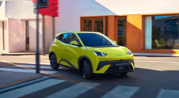 Żółty BYD Dolphin Surf sunie ulicą, niczym mewa nad wodą, w letni dzień.