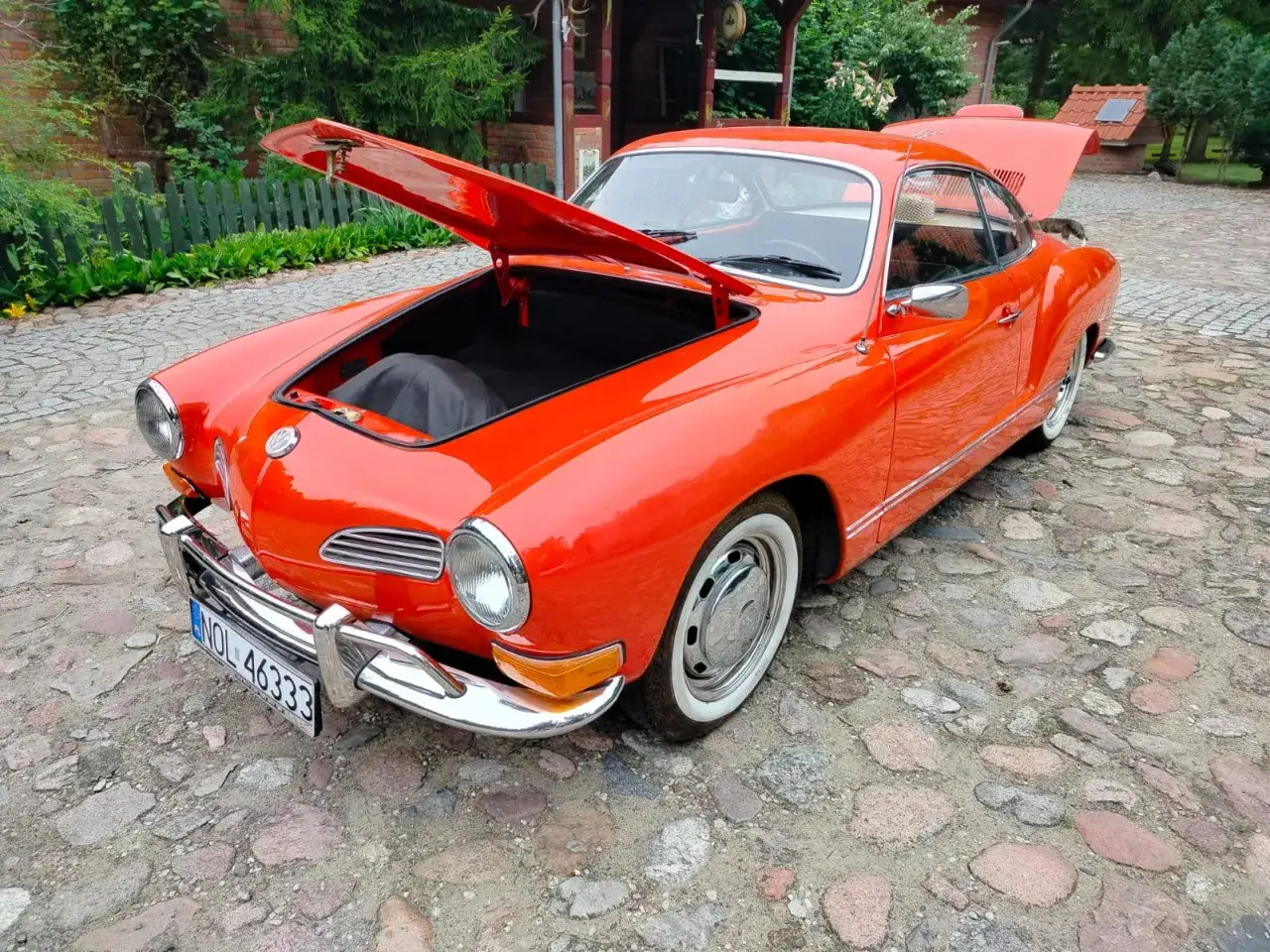 Pomarańczowy Karmann Ghia z otwartą maską i bagażnikiem, gotowy na podróż.