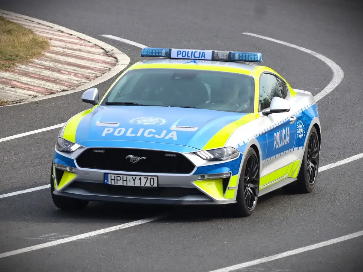 Ford Mustang w barwach policji pędzi po torze wyścigowym.