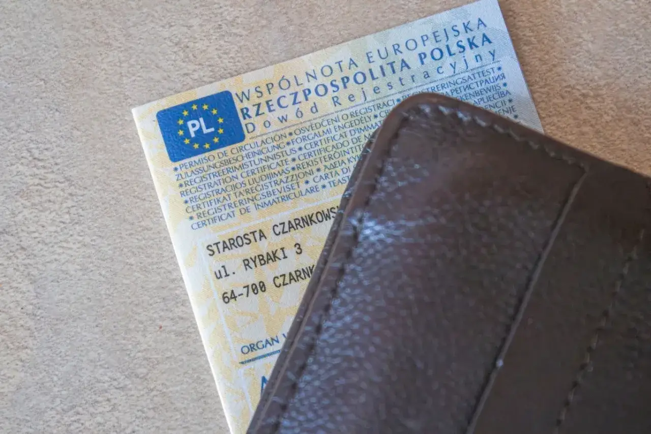 Dowód rejestracyjny pojazdu, obok brązowego portfela. Czy trzeba mieć przy sobie dowód rejestracyjny? Tak, jest to dokument potwierdzający Twoje prawo do poruszania się pojazdem.