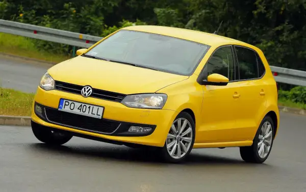 Żółty Volkswagen Polo 6R na mokrej drodze, z tablicą rejestracyjną PO 401LL.