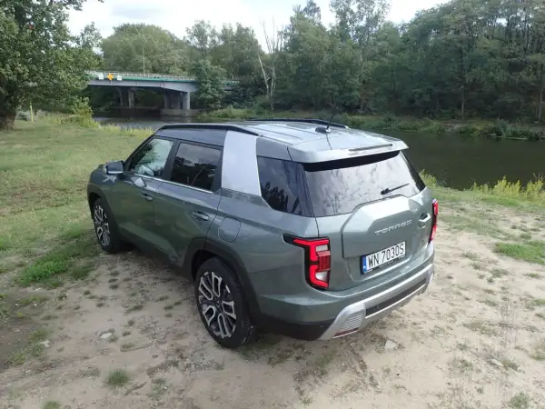 Zielony Torres auto zaparkowany nad rzeką, w tle most i las.