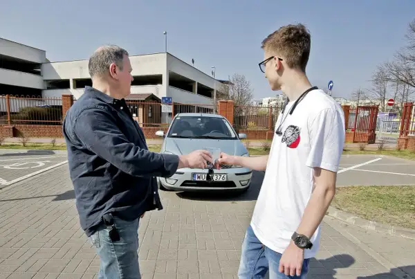 Mężczyźni przekazują sobie kluczyki do samochodu, co symbolizuje umowę użyczenia.