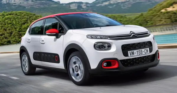 Biały Citroen C3 2025 z czerwonym dachem i lusterkami pędzi po drodze, otoczony zielonymi wzgórzami.