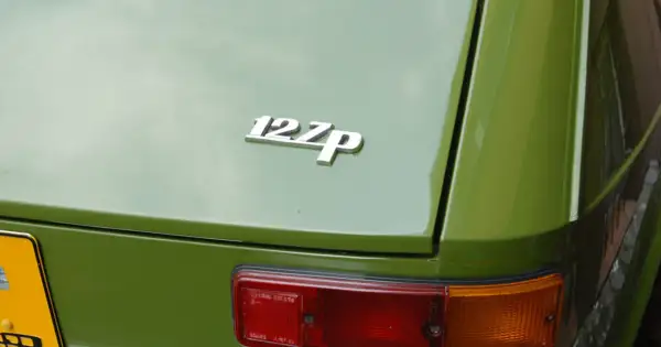 Chromowana plakietka "127p" na zielonej karoserii klasycznego Fiata 127. Widoczny fragment tylnej lampy.