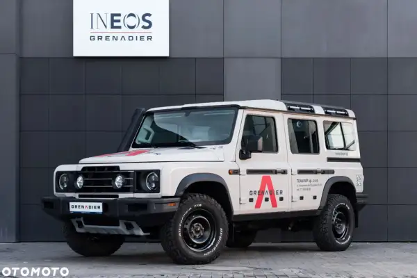 Beżowy INEOS Grenadier z czerwonym logo "A" na drzwiach. Sprawdź INEOS Grenadier cena i możliwości tego terenowego SUV-a.