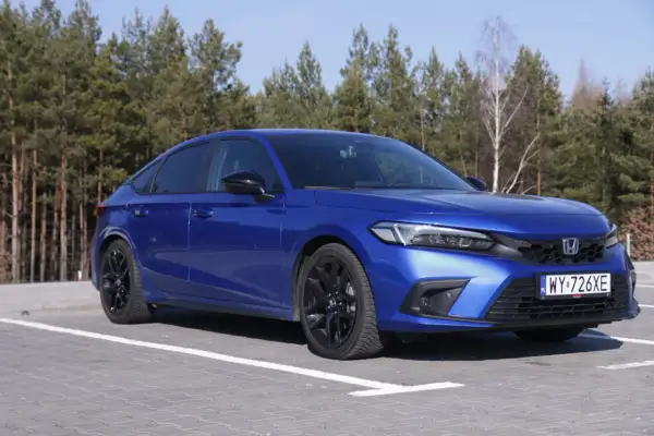 Błękitny Honda Civic 11. generacji z czarnymi felgami zaparkowany na tle lasu.
