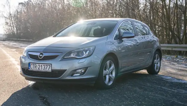 Szary Opel Astra J 1.4 Turbo na tle drzew i słońca.