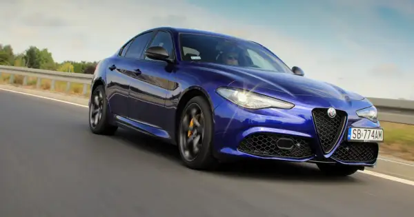 Błękitne Alfa Romeo Giulia Veloce pędzi po drodze, błyszcząc w słońcu.