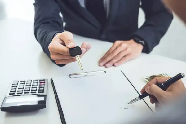 Przekazanie kluczyków do samochodu po podpisaniu umowy leasingu finansowego. Obok kalkulator i pieniądze.