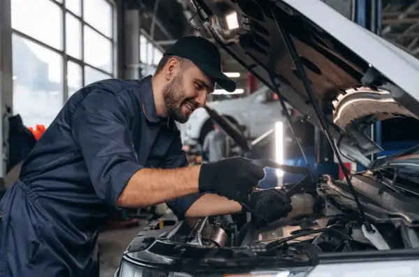Uśmiechnięty mechanik w warsztacie sprawdza silnik. Zastanawiasz się, ile zarabia mechanik?