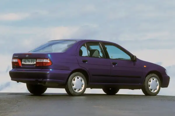 Fioletowy Nissan Almera z lat 90. stoi na tle błękitnego nieba.